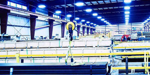 Marmon Keystone A brightly lit industrial warehouse interior with stacked tube pipes and metals, yellow safety railings, and a hoist system hanging from the ceiling, showcasing a busy supplychain distributor environment.