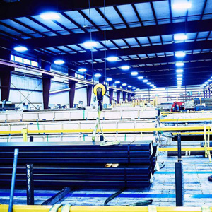 Marmon Keystone A brightly lit industrial warehouse interior with stacked tube pipes and metals, yellow safety railings, and a hoist system hanging from the ceiling, showcasing a busy supplychain distributor environment.