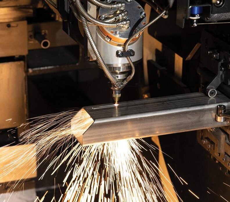 Marmon Keystone A CNC laser cutting machine emits sparks while slicing through a metal rectangular tube, showcasing precision manufacturing essential for supplychain distributor operations in an industrial setting.